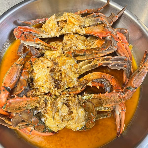 Steamed blue crabs in a metal bowl, covered in a rich, buttery sauce with garlic and spices.