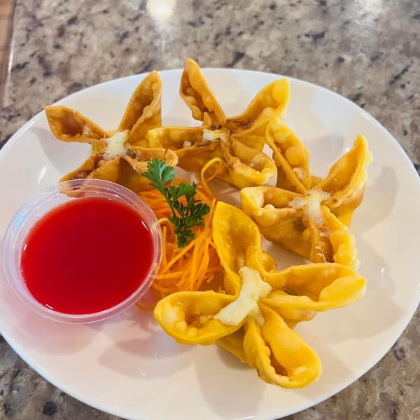 Crab rangoons with sweet chili sauce and shredded carrots on a white plate at Juicy Seafood Mayport.