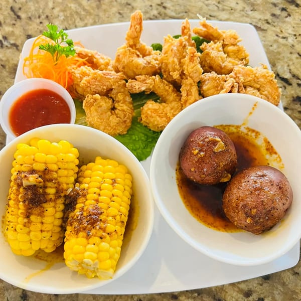 A platter of crispy fried shrimp, corn on the cob, red potatoes, and a side of dipping sauce.