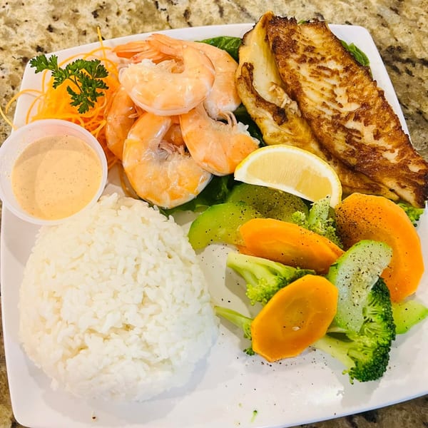 A seafood platter with grilled fish, shrimp, rice, steamed vegetables, and a side of sauce.