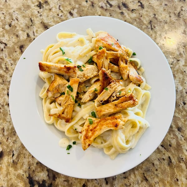 Creamy fettuccine alfredo topped with grilled chicken and fresh parsley on a white plate.